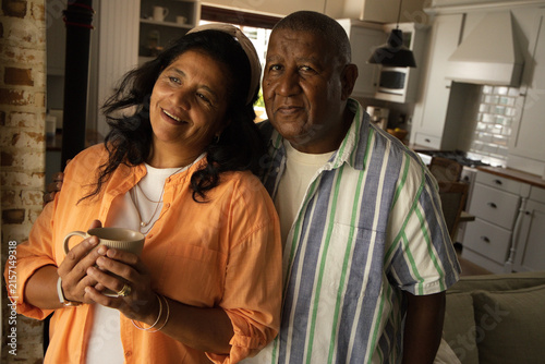 Mature African American couple standing in warm home kitchen holding ceramic mug and jewelry