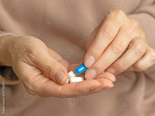 A close-up of a woman's hands holding a blue capsule and white pills. Daily dose of vitamins and mineral supplements. Healthcare, pharmaceuticals, and medicine concept.