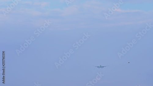 Passenger airplane descending and preparing for landing against a pale blue sky with light clouds, distant front view, static shot