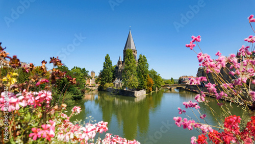 Temple Neuf standing on island in Moselle river, surrounded by trees and colorful flowers