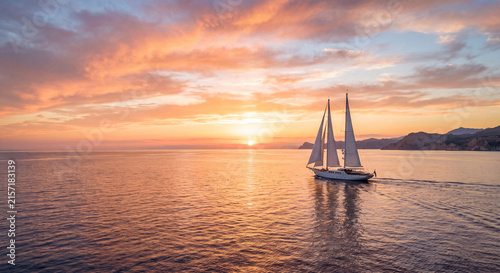 Sailing yacht at sunset, luxury sailboat sailing on calm ocean water during golden sunset, romantic sea landscape with sun reflections, serene nautical travel and cruise concept.
