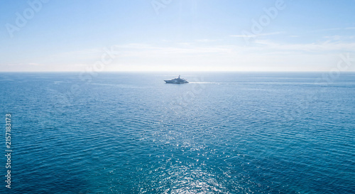 Luxury yacht in open sea, distant ship cruising on calm blue ocean horizon, wide aerial view of expensive motorboat vessel, peaceful Mediterranean travel and nautical leisure concept.
