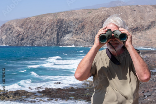 Foto Mature adult man with white hair and beard actively observing the vast ocean and