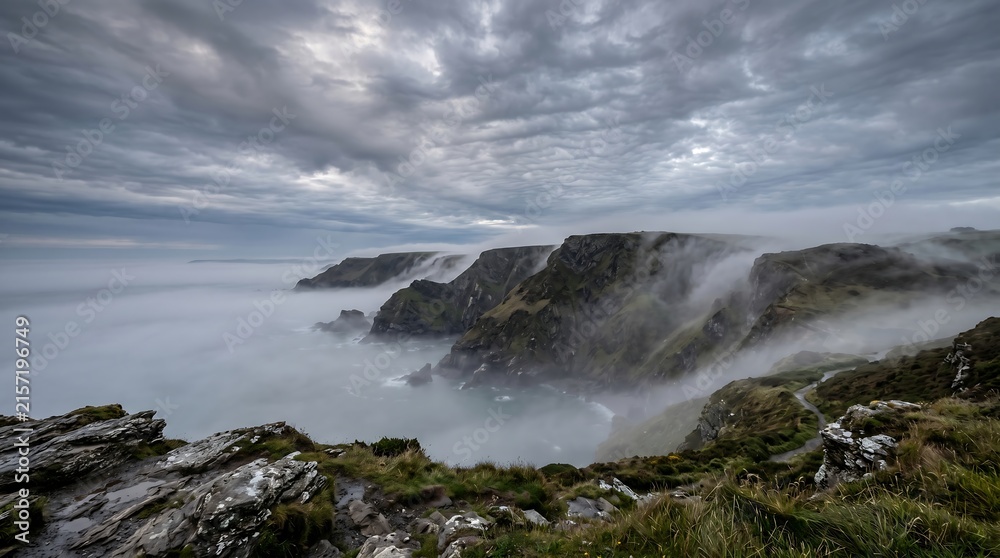 Fototapeta premium Coastal British sea fog creeping over Devon cliffs in early morning grey light.