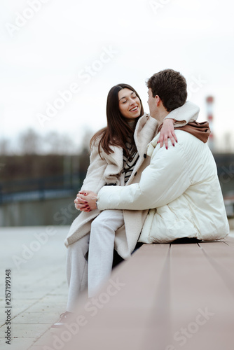 Bild auf Leinwand Couple sitting on a bench in winter clothing enjoying a romantic moment outdoors