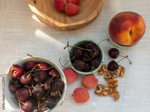 Quadro su tela Fresh sweet cherries, Prunus avium, lychee fruit, Litchi chinensis, ripe peach, Prunus persica, and walnut kernels, Juglans regia, arranged on light linen