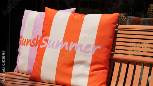 Fotografie Decorative pillows with bold stripes and with text summer are placed on a slatted wooden bench, evoking a warm weather vibe and summer concept