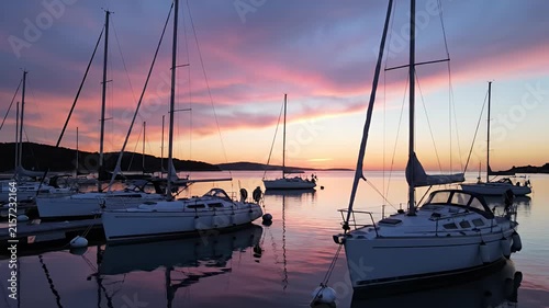Sailboats moored in calm harbor at pink sunset