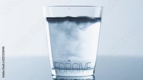 Black ink poured into a glass of clear water dissolves the word regret revealing the word forgive in a conceptual display of letting go