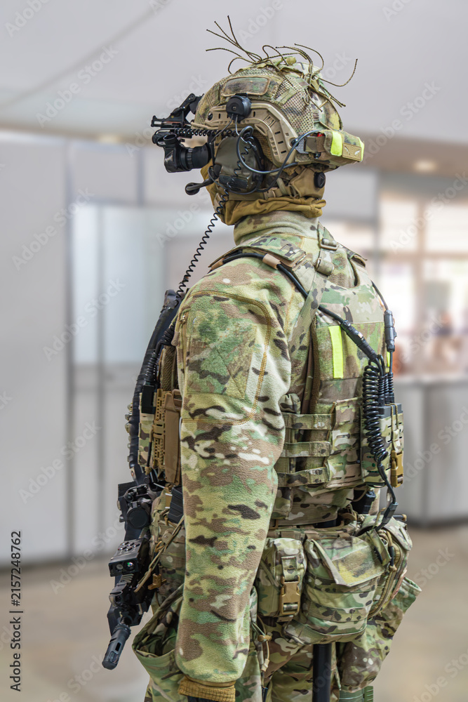 Fototapeta premium Mannequin in camouflage uniform, side profile view, tactical vest with pouches, helmet with communication device, blurred industrial background, even diffused lighting, muted earthy tones, military