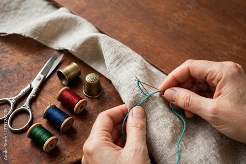 Hands Sewing Fabric with Thread and Scissors on Wood
