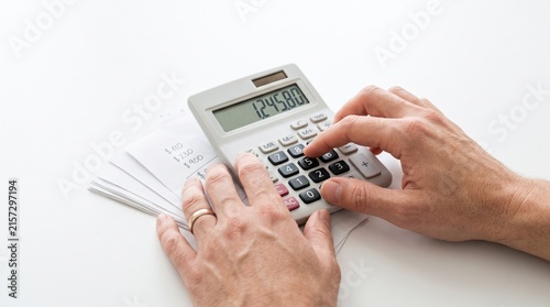 Person using a calculator to tally financial figures on paper with a white background