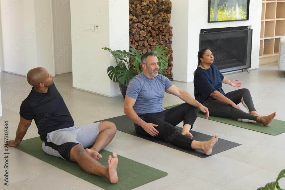 Naklejka premium Diverse adults wearing workout wear stretching on green and dark mats in living room with fireplace
