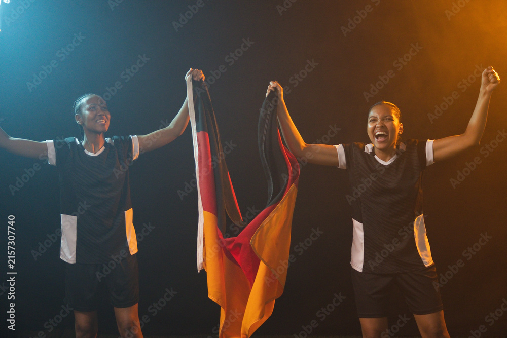 Fototapeta premium African female team wearing black-white jerseys holding black-red-gold flag raising arms onstage