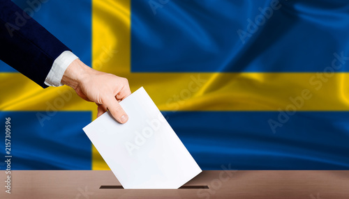 Bild auf Leinwand Hand placing a ballot in ballot box with the Swedish flag in the background