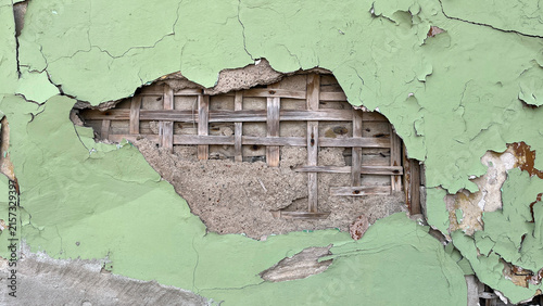 Obraz na plátně Close‑up of a weathered green plaster wall with extensive peeling paint and cracked render, exposing traditional wooden lath and deteriorated masonry beneath, revealing historic construction details