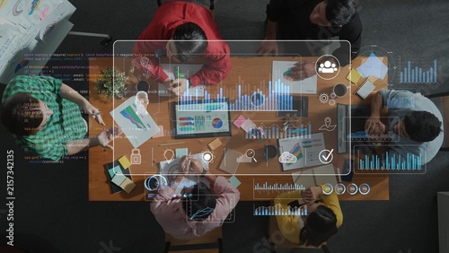 A diverse group of individuals collaborates at a wooden table  analyzing data and creating visual presentations with digital tools and charts for effective teamwork. Raster
