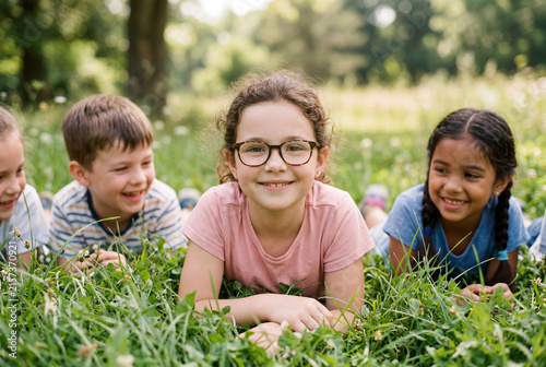 Group of diverse children lie down together in green grass outdoors