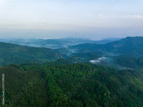 Foto Aerial view of layered forested mountain ranges shrouded in soft mist under a pale hazy morning sky, showcasing natural depth and serenity