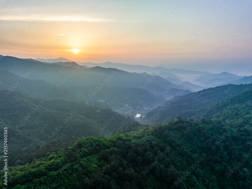 Fototapeta premium A serene landscape of layered forested mountains at sunrise, with mist drifting through valleys under a soft warm sky.