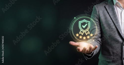 Businessman holding glowing quality assurance shield icon representing digital service excellence standards with holographic five star customer feedback interface display