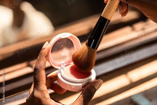 Obraz na plátne Close-up of hands applying blush with a makeup brush in natural light