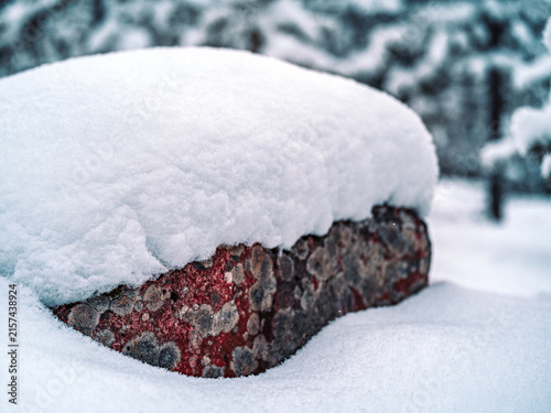 Close-up of a large rock covered by a thick layer of fresh snow in a Nordic winter forest, showing the textured stone beneath the snow.