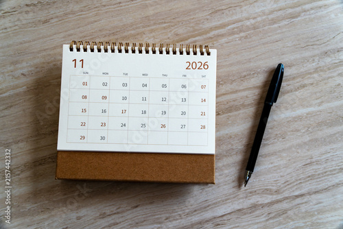 November 2026 desk calendar with a black pen on a light textured wooden background. Minimal overhead view for agenda and planning concept.
