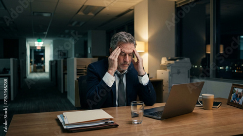 Stressed businessman with headache working late at office desk with laptop