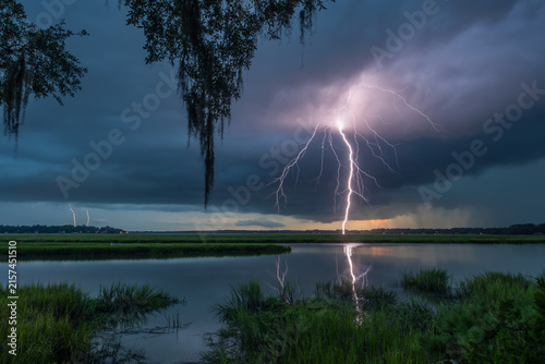Lightning strikes over Beaufort SC wetlands during a dramatic evening storm with dark clouds and tall grass