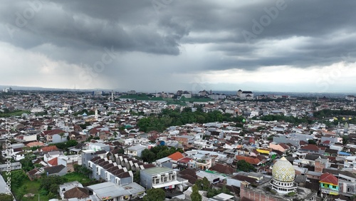 Obraz na plátně A wide high-angle landscape view of a sprawling coastal city and residential neighborhood under a dramatic stormy sky filled with dark rain clouds