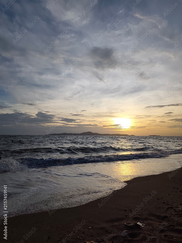 Obraz premium Golden sunset over dark sea waves washing onto sandy beach shore.