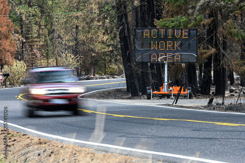 Red Vehicle Passes Wildfire Warning Sign on Road Through Burned Forest