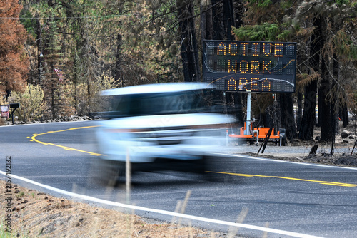 White Vehicle Passes Wildfire Warning Sign on Road Through Burned Forest