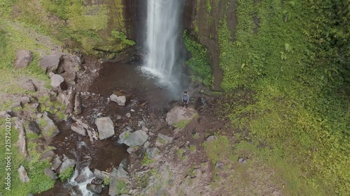 A Serene Portrait of Solitude Beneath a Majestic Waterfall in a Lush Green Landscape