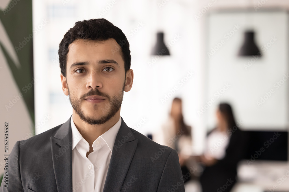 Fototapeta premium Headshot portrait young adult team member stands confidently in office, colleagues in background, represents business leadership, corporate professionalism, career growth. Human resources, employment