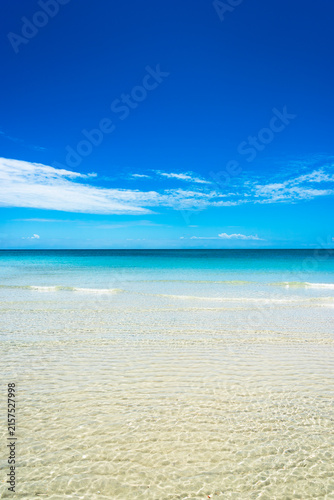 Crystal clear turquoise water over sandy seabed with a bright blue sky on a tropical beach paradise.