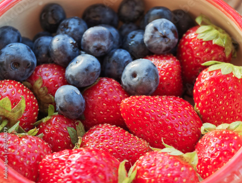 A bowl filled with ripe strawberries and blueberries sits on a kitchen counter during midday. The fruit is ready to be enjoyed as a healthy snack