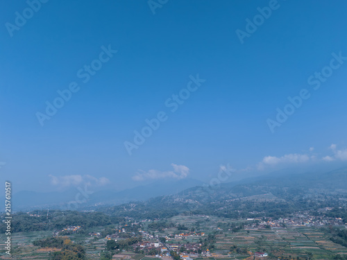 Vast blue sky over a hazy mountain range, distant hills, and rural settlements nestled in the valley.