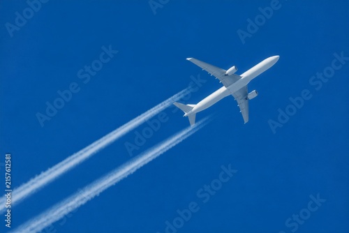 Commercial airplane leaving contrails flying through clear sky