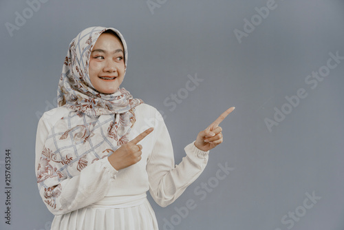 Portrait happy young asian muslim female standing on isolated pointing finger hands to blank space for text advertisement. Beautiful Attractive Muslim woman wearing hijab fashion costume.