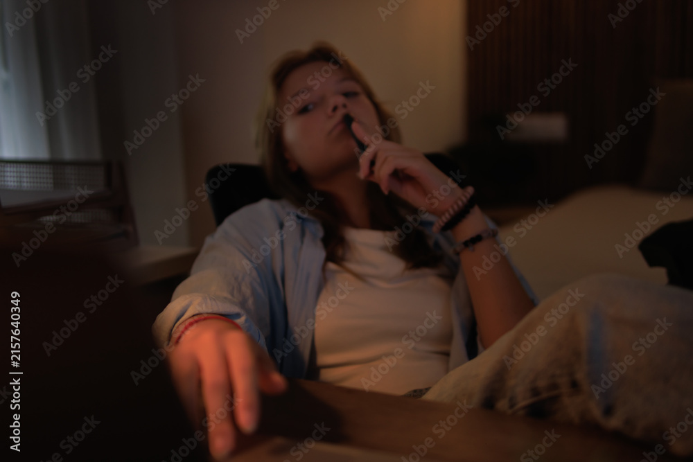 Obraz premium Young woman student focused and engaged in deep thought while studying or working late at night, holding a pen near her mouth, wearing casual clothes at a desk