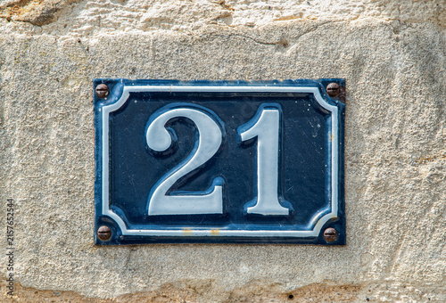 Blue and white house number 21 plaque mounted on a textured traditional stone wall.