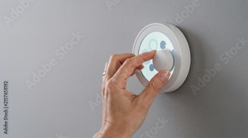 Smart home thermostat control, hand adjusting digital temperature dial on wall, modern climate automation system for energy efficiency