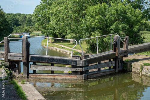 Traditional wooden lock gates on a peaceful navigable canal surrounded by green countryside in rural England.