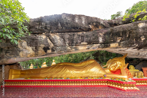 Photography Massive golden reclining Buddha statue sheltered beneath a large natural rock cliff overhang
