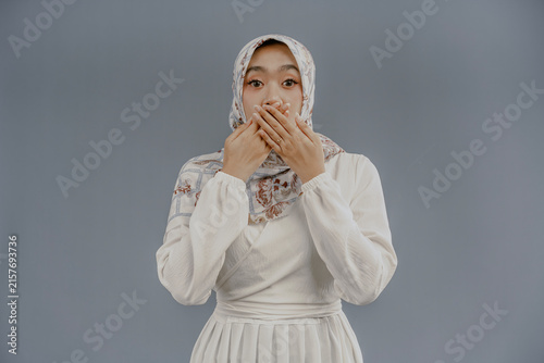 Принти на полотні Oops! Surprised young Asian Muslim female covering her mouth with hands and staring at camera while standing against white background