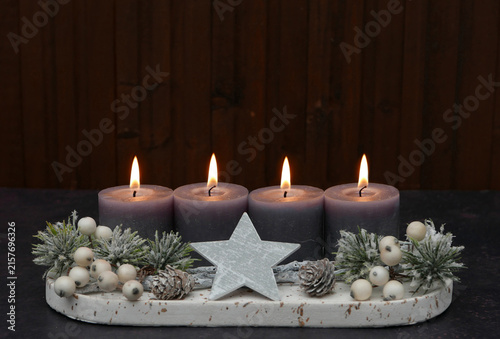 Fourth Sunday of Advent: Advent arrangement with berries, twigs, and four lit candles against a wooden background, with space for text.