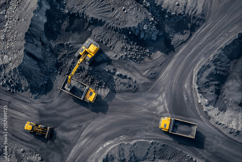 Aerial view of heavy excavation machinery loading and hauling dark mineral material across a rugged industrial quarry.