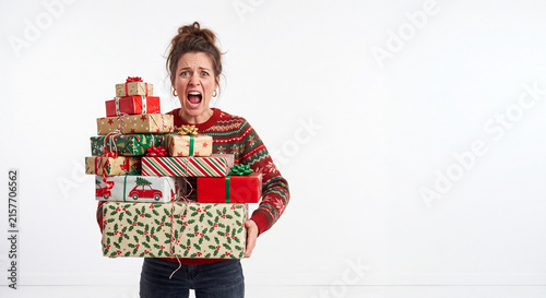 A funny stressed young woman carrying an enormous pile of wrapped holiday gift boxes while shouting against a white background